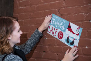 Woman Applying "Christmas Sale"  ClingZ Vinyl Wall Graphic to a Brick Wall