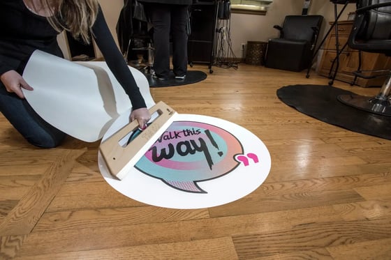 woman removing application tape from a walk on vinyl floor graphic installed on a wood floor