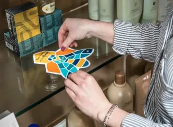 person installing a vinyl graphic to a glass product shelf
