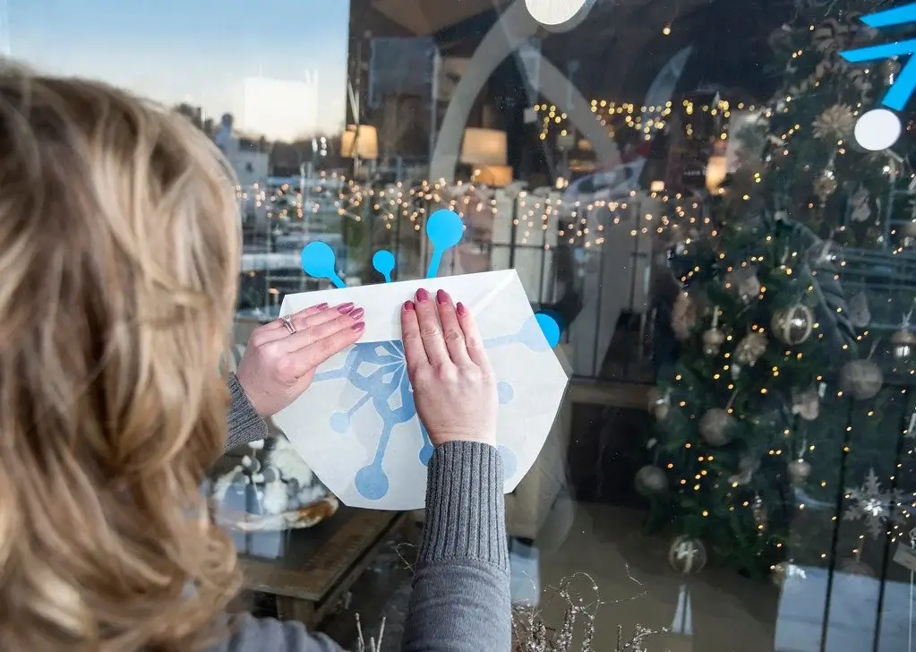 person removing application tape from a snowflake vinyl window graphic to a storefront window