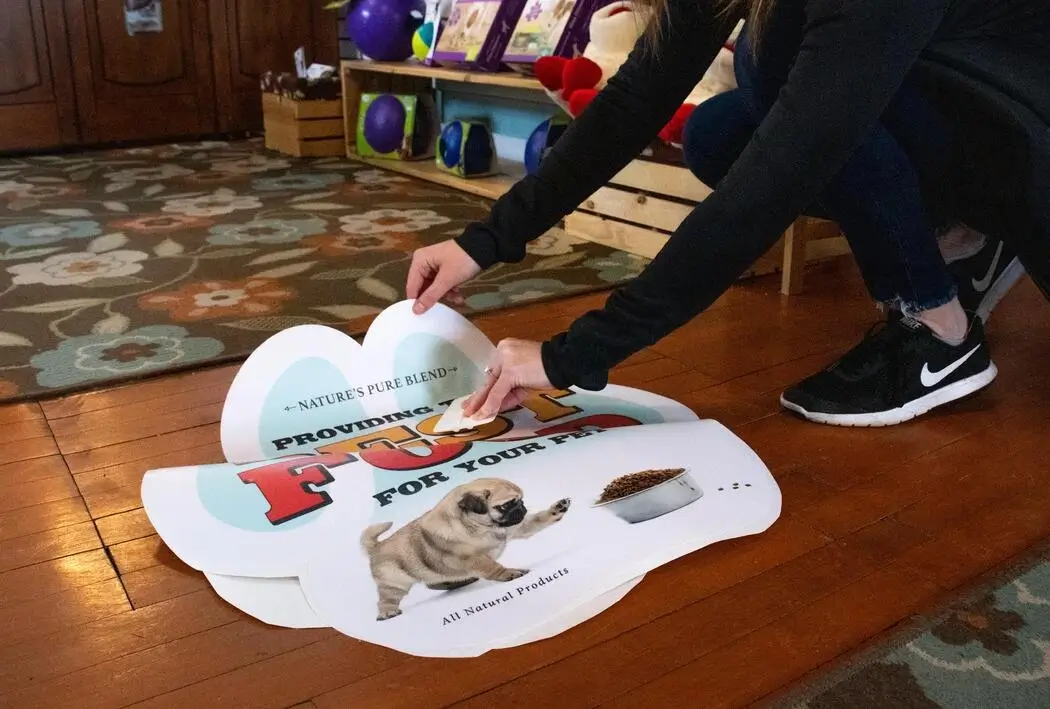 Person applying a walk on floor graphic with a overlaminate film to a wooden floor.
